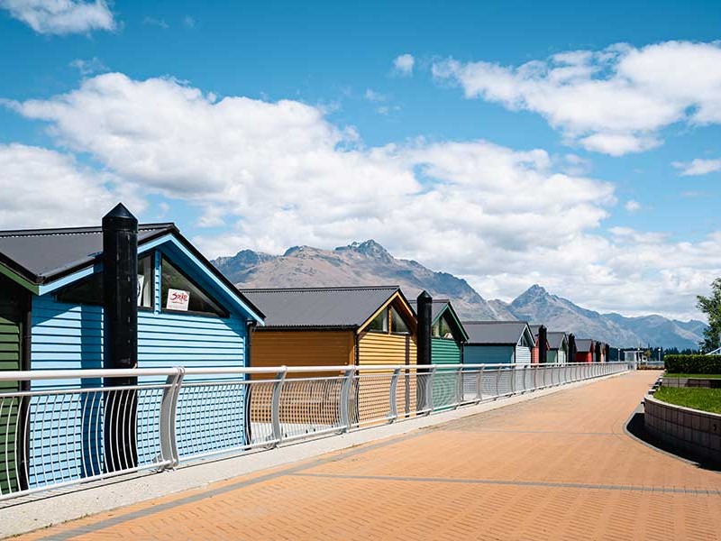 Colourful boatsheds along the Frankton Marina boardwalk, Queenstown, with The Remarkables behind